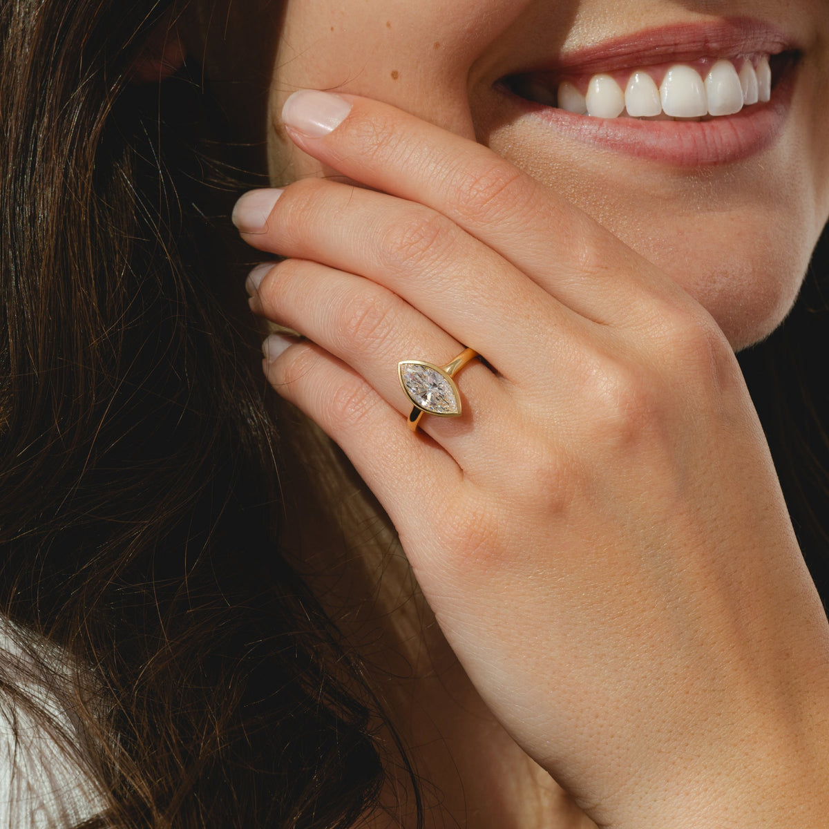 A yellow gold ring featuring a marquise cut diamond center stone in a bezel setting.